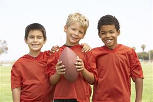 Three youth football players smiling holding a football