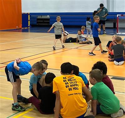 A CIT sits on the gym floor surrounded by young children.