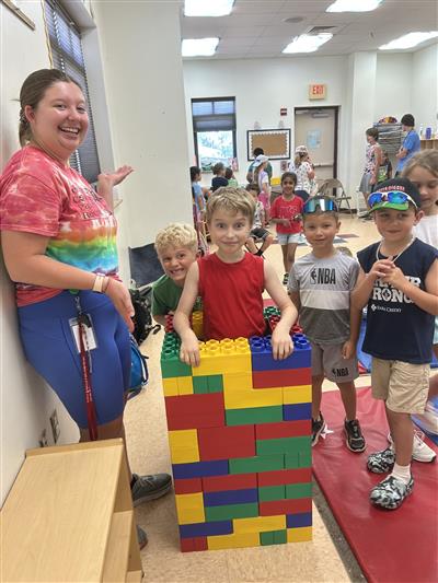 Camper counselor and campers standing around a giant Lego tower and smiling.
