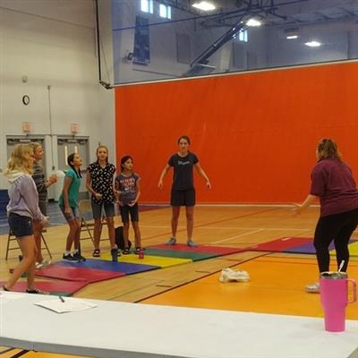 6 children stand in a semi-circle with arms drawn back and fisted grimacing with an adult instructor standing in front of them modeling.